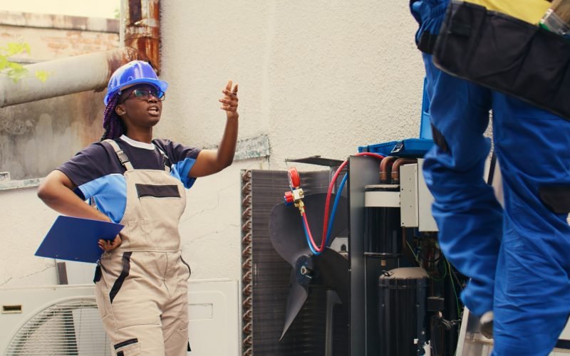 Diverse team of adept repairman brainstorming possible ways to recondition busted outdoor air conditioner. Knowledgeable professionals commissioned by home owner to patch up broken condenser